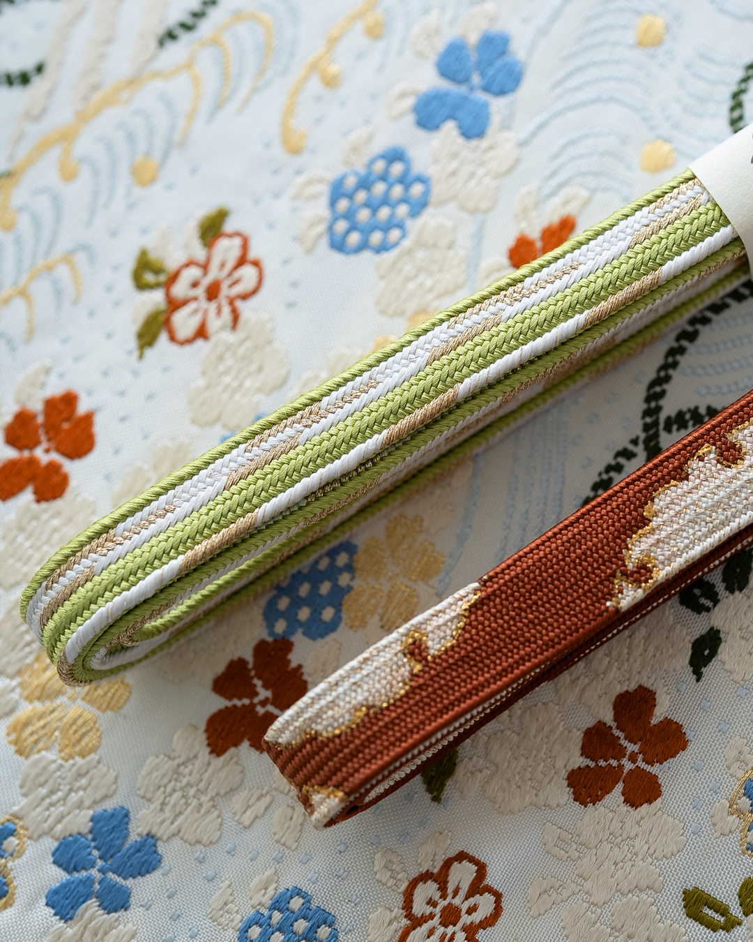 ＜お仕立て代込＞勝山さと子 「流水花束紋」 九寸名古屋帯 桜草木 / 白・灰水色と橙に金糸 の画像